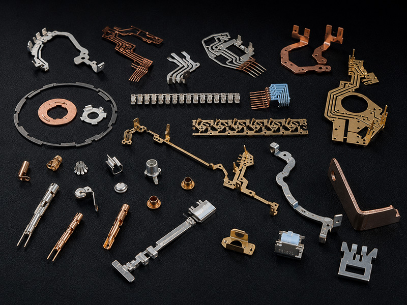 EMG_Präzise Metallkomponenten auf schwarzem Untergrund Auf einer schwarzen Fläche sind verschiedene kleine, filigrane elektronische Bauteile und Steckverbinder aus Metall und Kupfer angeordnet. Die Teile unterscheiden sich in Form und Größe und zeichnen sich durch feine Details und präzise Verarbeitung aus.